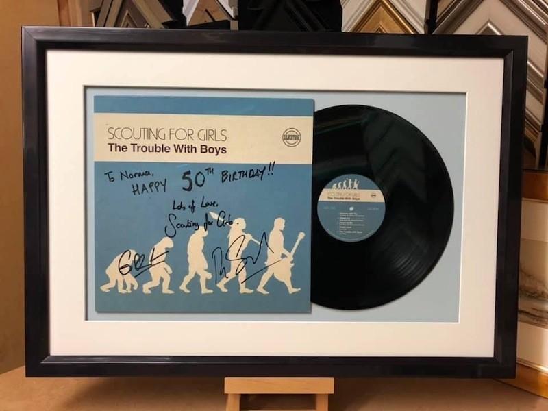 A signed Scouting for Girls record cover and album, framed with a gloss black box frame, mount and glazed with Tru Vue reflection control glass.